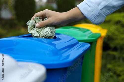 Woman throwing crumpled tissue into recycling bin outdoors, closeup