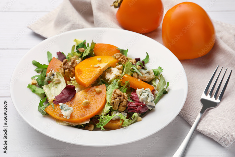 Delicious persimmon salad and fork on white wooden table Delicious persimmon salad and fork on white wooden table