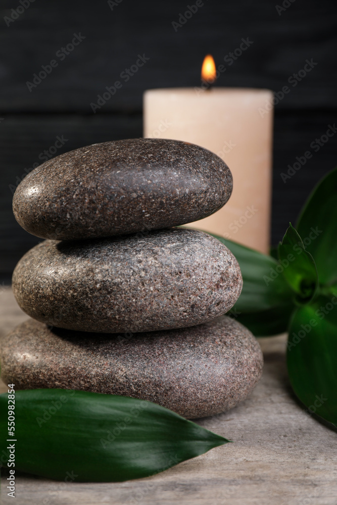 Obraz premium Stacked spa stones with bamboo leaves and candle on wooden table, closeup