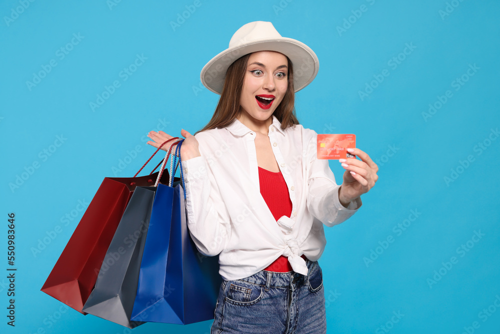 Excited young woman with shopping bags and credit card on light blue background Excited young woman with shopping bags and credit card on light blue background