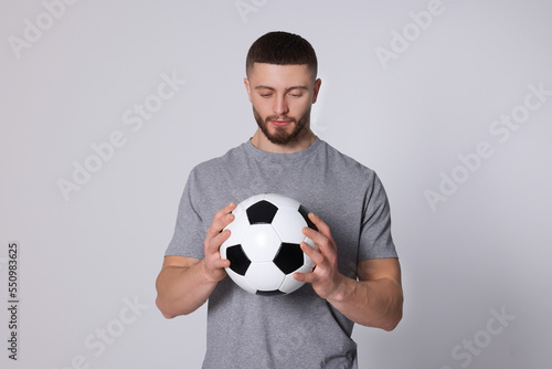 Athletic young man with soccer ball on light grey background