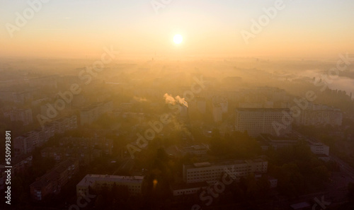 Forest park trees  river and many high-rise buildings in city in early morning at dawn in summer. Brightly shining sun  clear cloudless sky and morning mist Sunbeams and shadows Aerial drone landscape