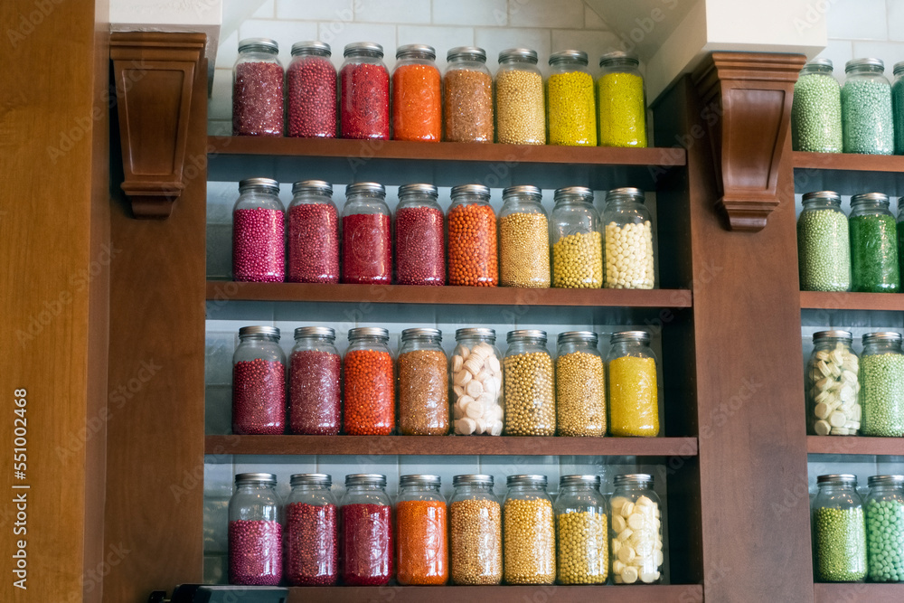 Candy toppings in jars on several shelves inside a confectionery shop or bakery