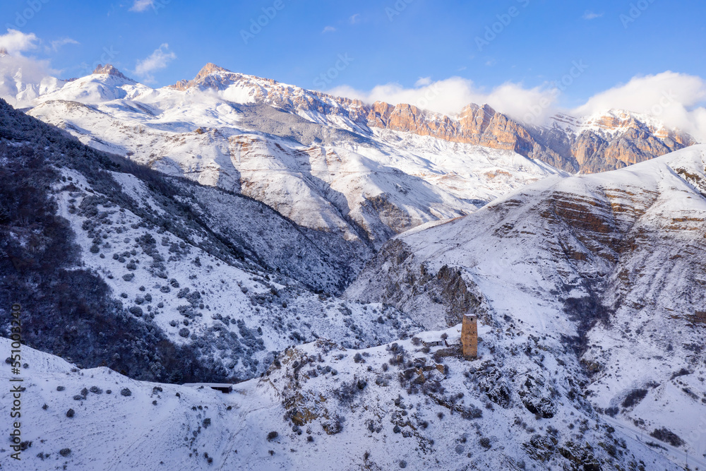Aerial view of Skalisty Mountain Range and old Ossetian tower in Makhchesk village on sunny winter day. Digoria, North Ossetia, Russia.