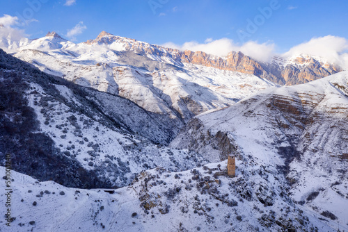 Aerial view of Skalisty Mountain Range and old Ossetian tower in Makhchesk village on sunny winter day. Digoria, North Ossetia, Russia.