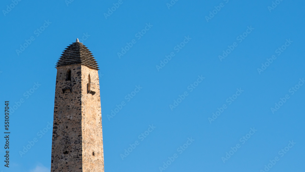 Old Ingush Ozdi tower on the background of blue sky on sunny winter day. Ingushetia, Caucasus, Russia.