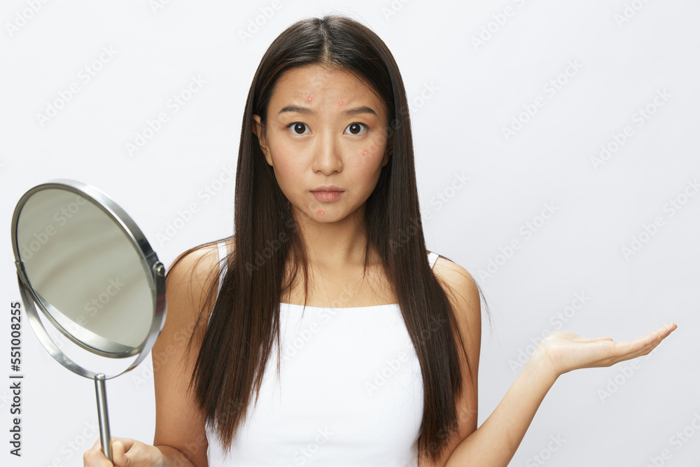 Asian woman with mirror in hand facial skin problems, acne and inflammation, red rash and allergies, chicken pox, sadness from rashes. Facial skin care concept for diseases and nerves Asian woman with mirror in hand facial skin problems, acne and inflammation, red rash and allergies, chicken pox, sadness from rashes. Facial skin care concept for diseases and nerves