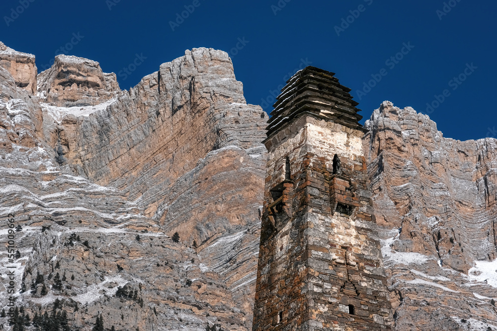 A tower of old Ingush towers complex Niy agains rocks of Skalisty Range on sunny winter day. Ingushetia, Caucasus, Russia.