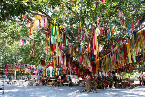 Ancient small shrine for thai people travelers travel visit respect praying deity angel and tie color fabric offerings to holy tree for blessing mystical on November 3, 2022 in Suphan Buri, Thailand © tuayai