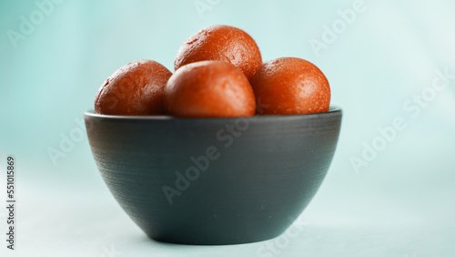 Sweet Gulab Jamun served in black ceramic bowl, Famous Indian dessert sweets isolated over blue indoor studio background