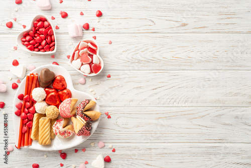 Valentine's Day celebration concept. Top view photo of heart shaped saucers with chocolate jelly candies and cookies on white wooden desk background with copyspace