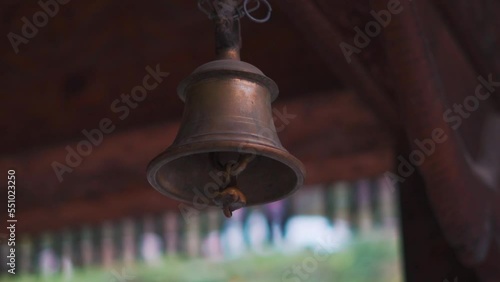 Closeup shot of brass or copper bell hanging from a chain at Tripura Sundari temple in Naggar near Manali in Himachal Pradesh, India. Temple bell in the temple in India. Religious background.  photo