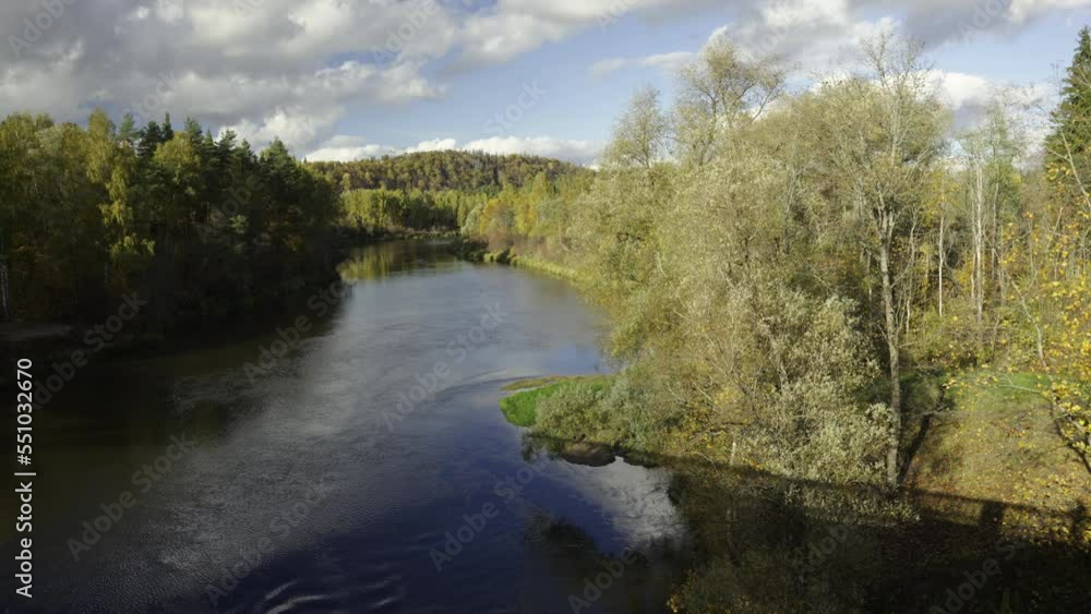 Bridge over the river Gauja in Sigulda. Autumn warm day in Latvia. National flags flutter against the backdrop of a vibrant park. Funicular against the background of white clouds in the blue sky. Bridge over the river Gauja in Sigulda. Autumn warm day in Latvia. National flags flutter against the backdrop of a vibrant park. Funicular against the background of white clouds in the blue sky.