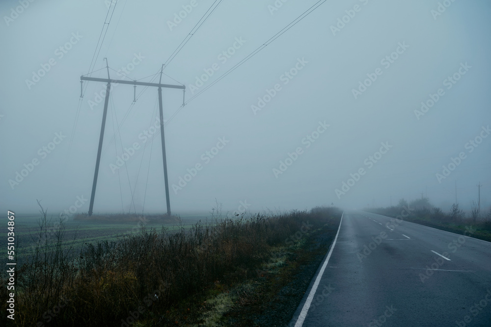 High-voltage pylons in the fog in the middle of a field, village