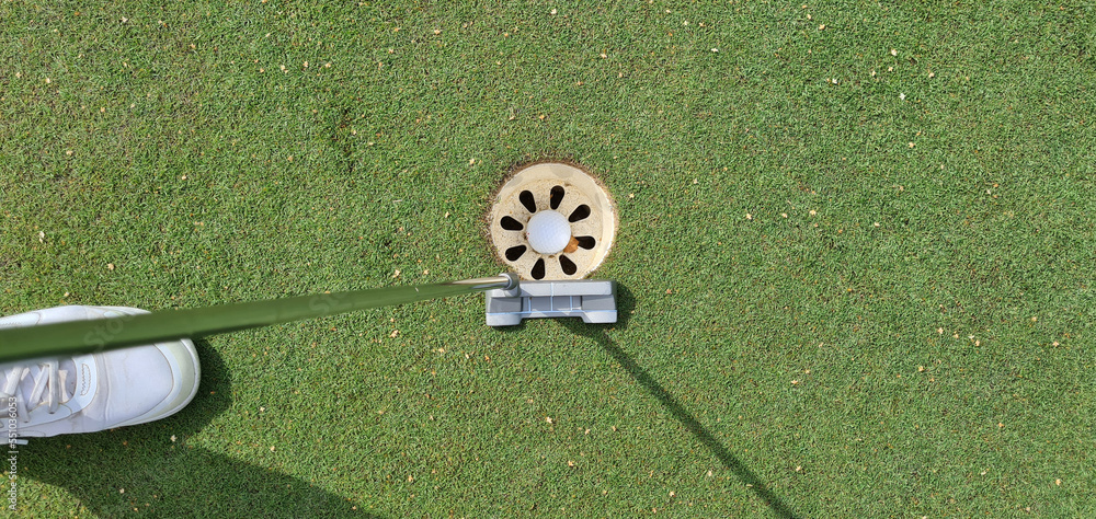 Obraz premium Golf player with putter and ball in hole on green