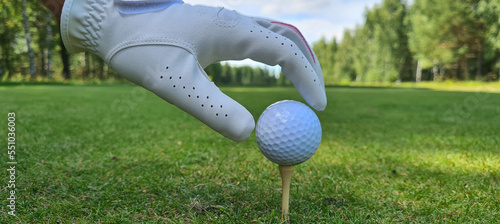 Hand holds golf ball with tee on golf course