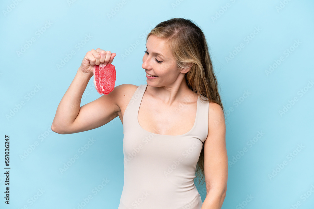 Young blonde woman holding a piece of meat isolated on blue background with happy expression Young blonde woman holding a piece of meat isolated on blue background with happy expression