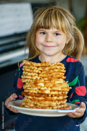 Portrait of happy little preschool girl holding fresh baked waffles. Smiling hungry toddler child with sweet biscuit wafer. Sweet sugar belgian waffles.