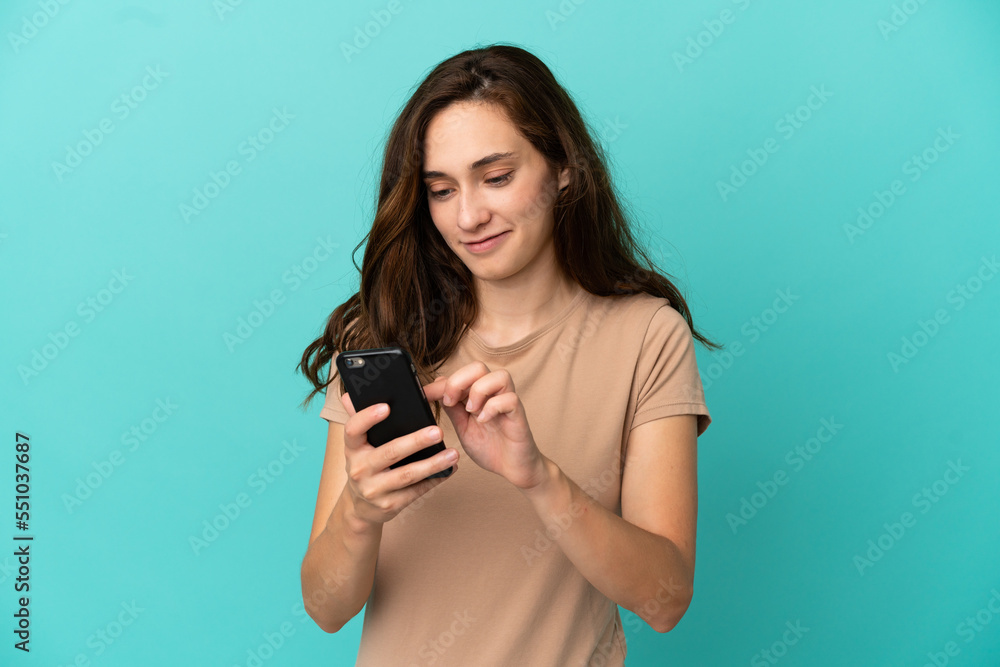 Young caucasian woman isolated on blue background sending a message or email with the mobile Young caucasian woman isolated on blue background sending a message or email with the mobile