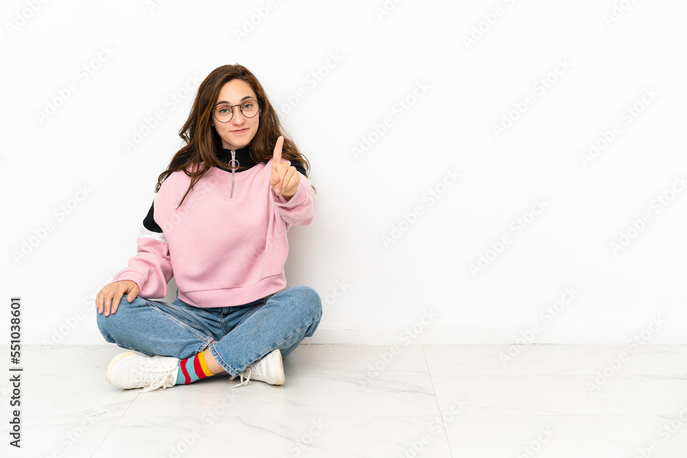 Young caucasian woman sitting on the floor isolated on white background showing and lifting a finger Young caucasian woman sitting on the floor isolated on white background showing and lifting a finger