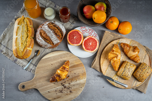 Bread, croissants, rolls, homemade yogurt, marmalade and honey jars, oranges, apples and sliced ​​grapefruit on the table in a rustic wooden bowl and wooden plate