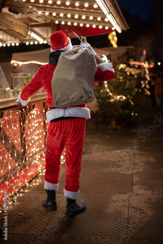 Portrait von einem verkleideten Weihnachtsmann, der auf einem Weihnachtsmarkt von Lichtern umgeben ist zur blauen Stunde 