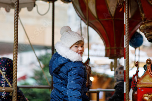 Little preschool girl riding on a merry go round carousel horse at Christmas funfair or market, outdoors. Happy child having fun on traditional family xmas market in Cologne, Germany