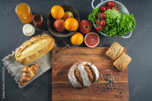 Scandinavian bread, croissant, pastries with sesame seeds, lettuce, cherry tomatoes, homemade yogurt, honey and marmalade, oranges, sliced ​​grapefruit,  on a wooden table, top view
