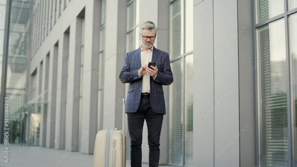 Confident mature businessman entrepreneur hold smartphone scrolling browsing during business trip official journey at modern office centre Successful man with suitcase luggage in classic suit outdoors Confident mature businessman entrepreneur hold smartphone scrolling browsing during business trip official journey at modern office centre Successful man with suitcase luggage in classic suit outdoors
