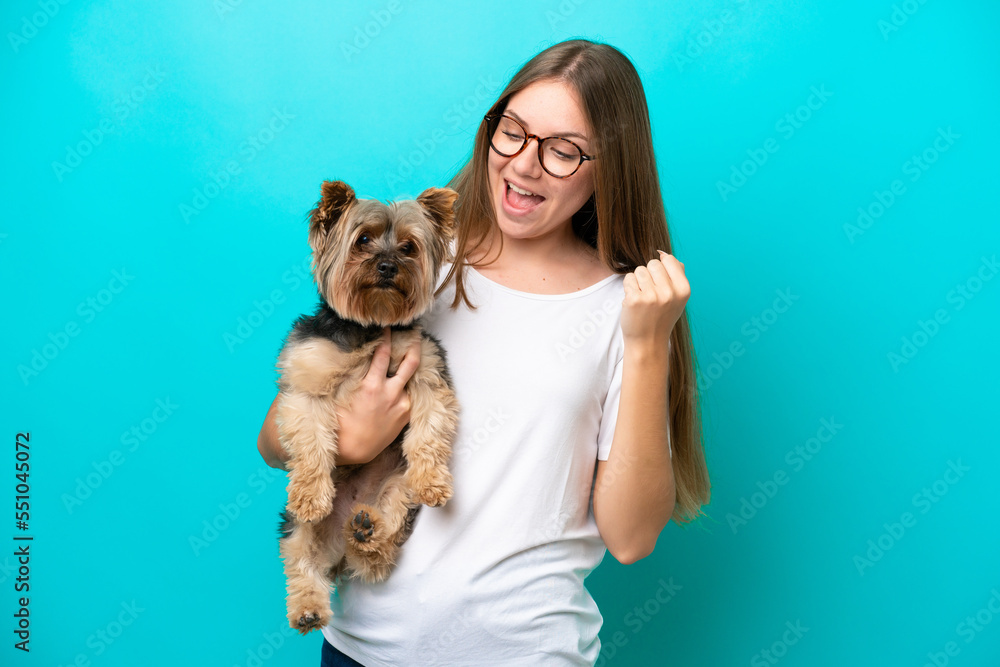Young Lithuanian woman holding a dog isolated on blue background celebrating a victory Young Lithuanian woman holding a dog isolated on blue background celebrating a victory