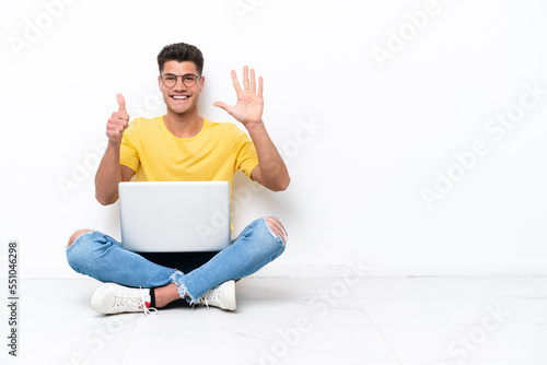 Young man sitting on the floor isolated on white background counting six with fingers