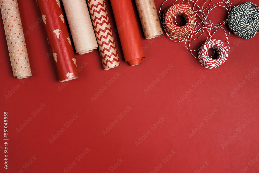 Christmas preparations with paper roll and decorative ropes on red background.