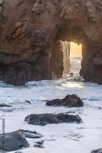 Stormy ocean water flowing through keyhole arch leaiving foam crests on the shores of Preiffer Beach around sunset.