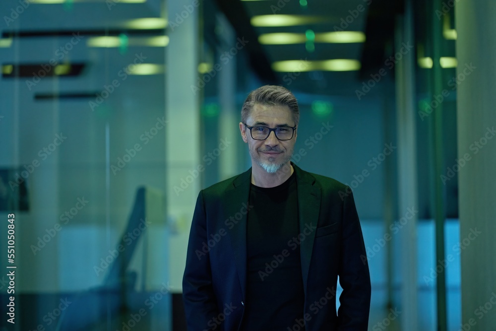 Fototapeta premium Business portrait - businessman standing on office corridor. Happy middle aged, mid adult, mature age man smiling. Entrepreneur in modern workplace. Copy space.