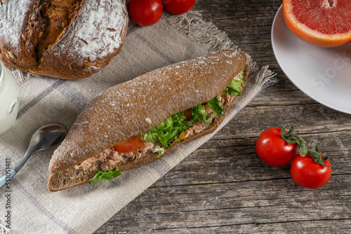 Tuna sandwich with letuce and tomato on woden table, fruits and vegetables. Colorful fresh group of vegetables and fruits. The concept of healthy eating.