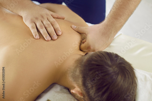 Professional masseur doing relaxing  pain relieving back massage for male patient. Relaxed young man enjoying remedial body massage at spa salon or physiotherapy treatment room. Cropped shot  close up