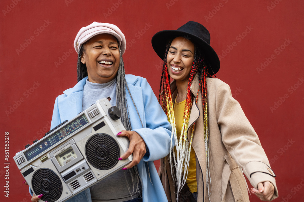 Happy African mother with her daughter having fun dancing and listening music with vintage boombox stereo