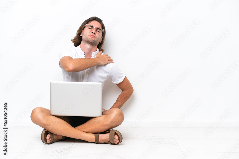 Young handsome man with a laptop sitting on the floor isolated on white background suffering from pain in shoulder for having made an effort Young handsome man with a laptop sitting on the floor isolated on white background suffering from pain in shoulder for having made an effort