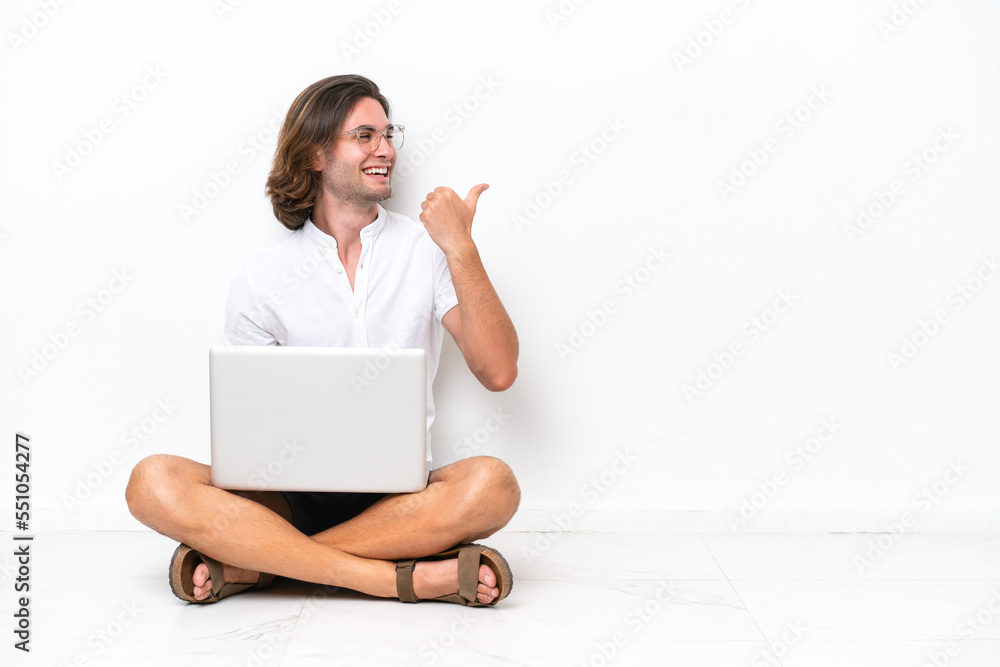Young handsome man with a laptop sitting on the floor isolated on white background pointing to the side to present a product Young handsome man with a laptop sitting on the floor isolated on white background pointing to the side to present a product