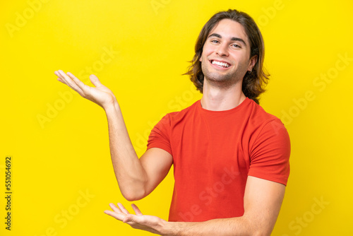 Caucasian handsome man isolated on yellow background extending hands to the side for inviting to come