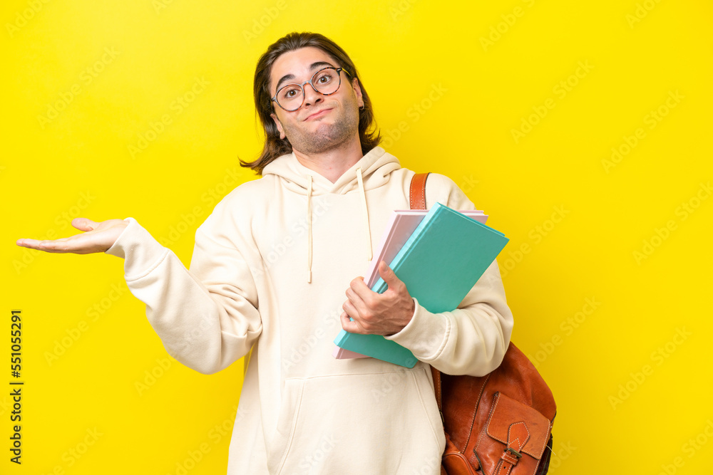 Young student handsome man isolated on yellow background having doubts while raising hands Young student handsome man isolated on yellow background having doubts while raising hands