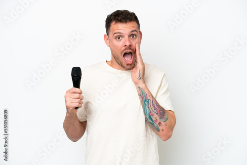 Young caucasian singer man picking up a microphone isolated on white background with surprise and shocked facial expression