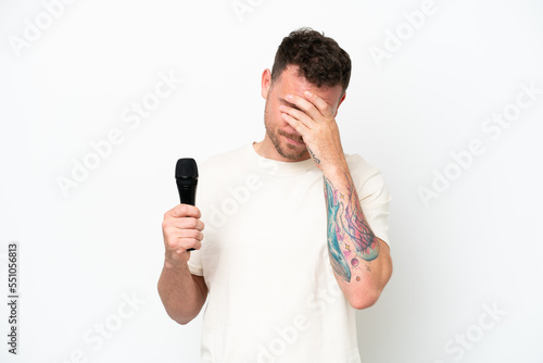 Young caucasian singer man picking up a microphone isolated on white background with tired and sick expression