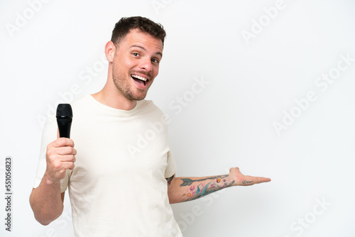 Young caucasian singer man picking up a microphone isolated on white background extending hands to the side for inviting to come