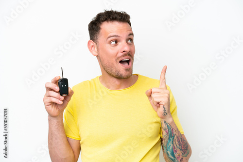 Young man holding car keys isolated on white background intending to realizes the solution while lifting a finger up