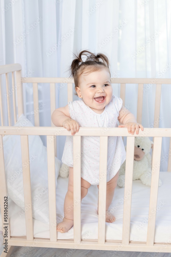 happy laughing baby girl in the crib in the nursery in a white bodysuit happy laughing baby girl in the crib in the nursery in a white bodysuit