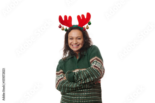 Cheerful woman in green Xmas patterned sweater and deer antler hoop, laughing looking at camera, posing with her arms crossed over white background with copy space. Happy atmosphere of winter holidays