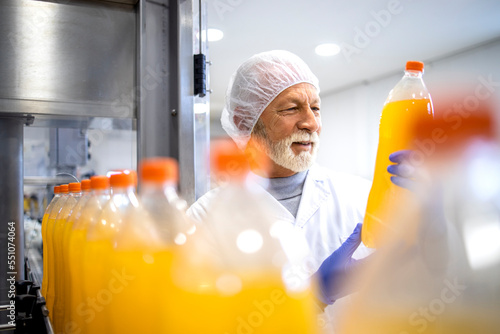 Fotografi Experienced factory worker holding PET bottle and doing visual inspection of orange juice in bottling plant