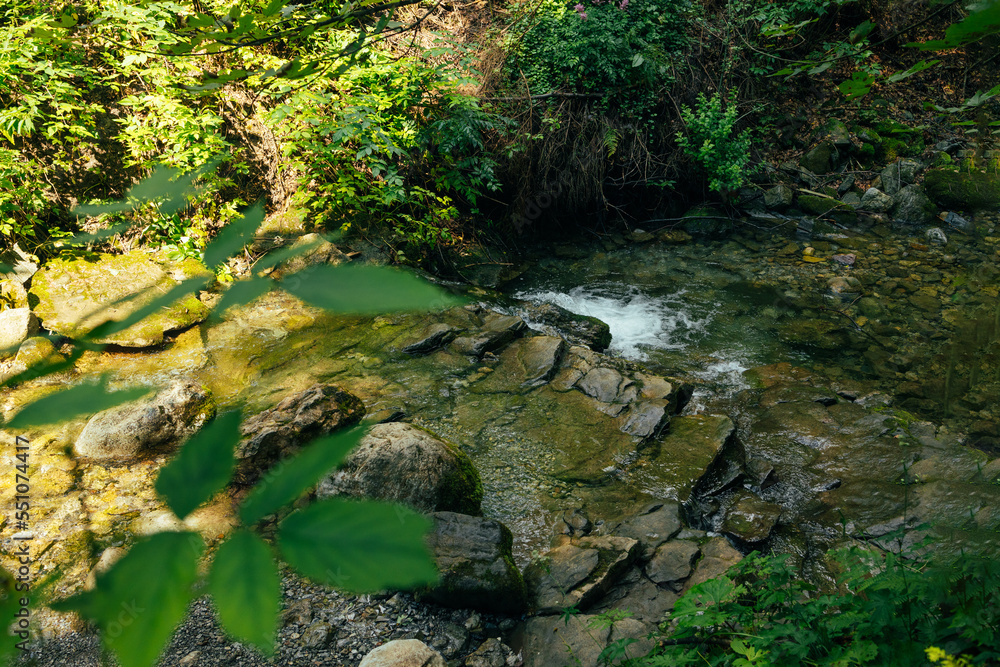 Cascade falls over mossy rocks. Mountain stream in green forest at spring time with sunbeams Cascade falls over mossy rocks. Mountain stream in green forest at spring time with sunbeams