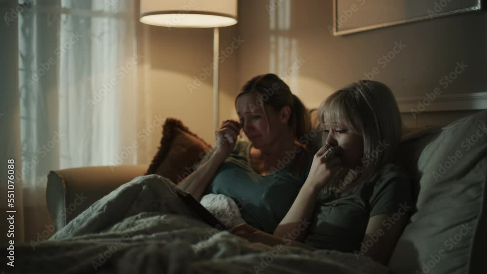 Crying mother and daughter on sofa streaming sad movie on digital tablet / Cedar Hills, Utah, United States Crying mother and daughter on sofa streaming sad movie on digital tablet / Cedar Hills, Utah, United States